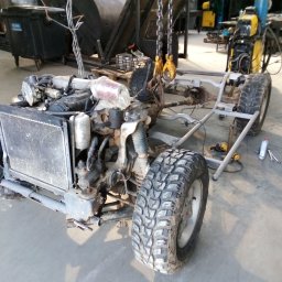 BCV SERWIS - MICHAŁ MAŁOLEPSZY - Podwozie samochodu terenowego z silnikiem, zawieszone na łańcuchu w warsztacie, widoczne narzędzia i spawarka w tle.