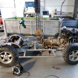 BCV SERWIS - MICHAŁ MAŁOLEPSZY - Podwozie terenowe z silnikiem, zawieszone na łańcuchach w warsztacie, obok skrzynia transportowa i zwinięty przedłużacz