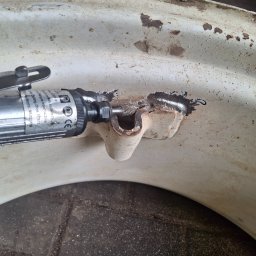 BCV SERWIS - MICHAŁ MAŁOLEPSZY - Szlifowanie skorodowanego elementu metalowego narzędziem pneumatycznym. Widoczne odpryski i ślady rdzy na powierzchni. Detal z bliska, ukazujący proces obróbki.