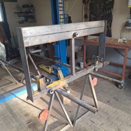 BCV SERWIS - MICHAŁ MAŁOLEPSZY - Spawana konstrukcja metalowa, rama na kozłach w warsztacie w Szarku. Widoczny podnośnik samochodowy i narzędzia.