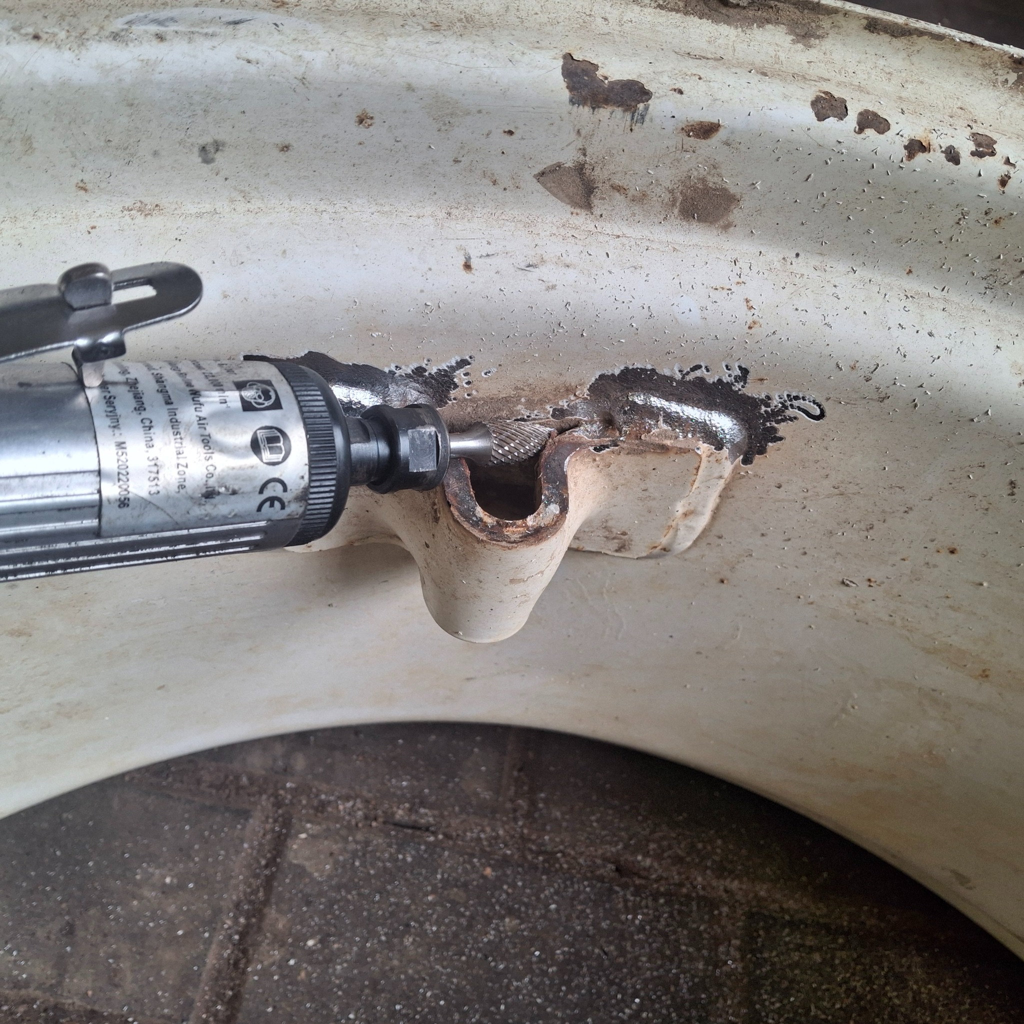 Szlifowanie skorodowanego elementu metalowego narzędziem pneumatycznym. Widoczne odpryski i ślady rdzy na powierzchni. Detal z bliska, ukazujący proces obróbki.