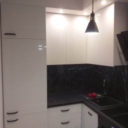 MARCIN MIROCHA - Nowoczesna kuchnia z białymi szafkami na wysoki połysk, czarnym blatem i marmurowym panelem ściennym, oświetlona wiszącą lampą z czarnym kloszem.