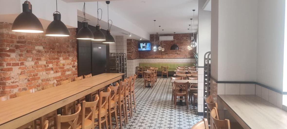 Wnętrze restauracji z długim stołem barowym, krzesłami barowymi, ceglaną ścianą i dekoracyjną podłogą.