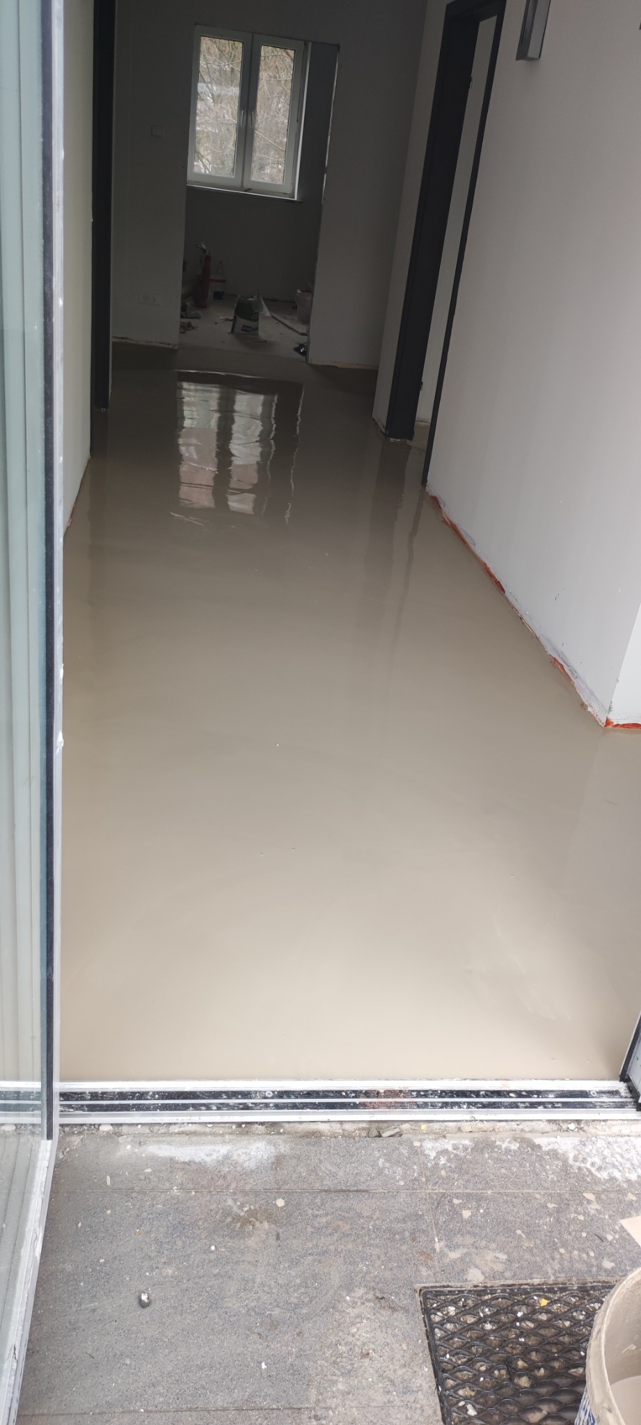 Wylewka samopoziomująca na podłodze w trakcie schnięcia, widoczne okno i drzwi balkonowe, przygotowanie do dalszych prac wykończeniowych.