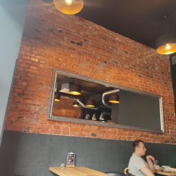 Horstbud - Wnętrze kawiarni z czerwoną cegłą na ścianie, dekoracyjnym lustrem w srebrnej ramie, widoczną instalacją sufitową i oświetleniem, oraz siedzącym mężczyzną przy stoliku.
