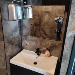 Horstbud - Nowoczesna łazienka z umywalką nablatową, czarną armaturą, marmurowymi płytkami na ścianach, dwoma srebrnymi suszarkami do rąk i odbiciem osoby w lustrze.