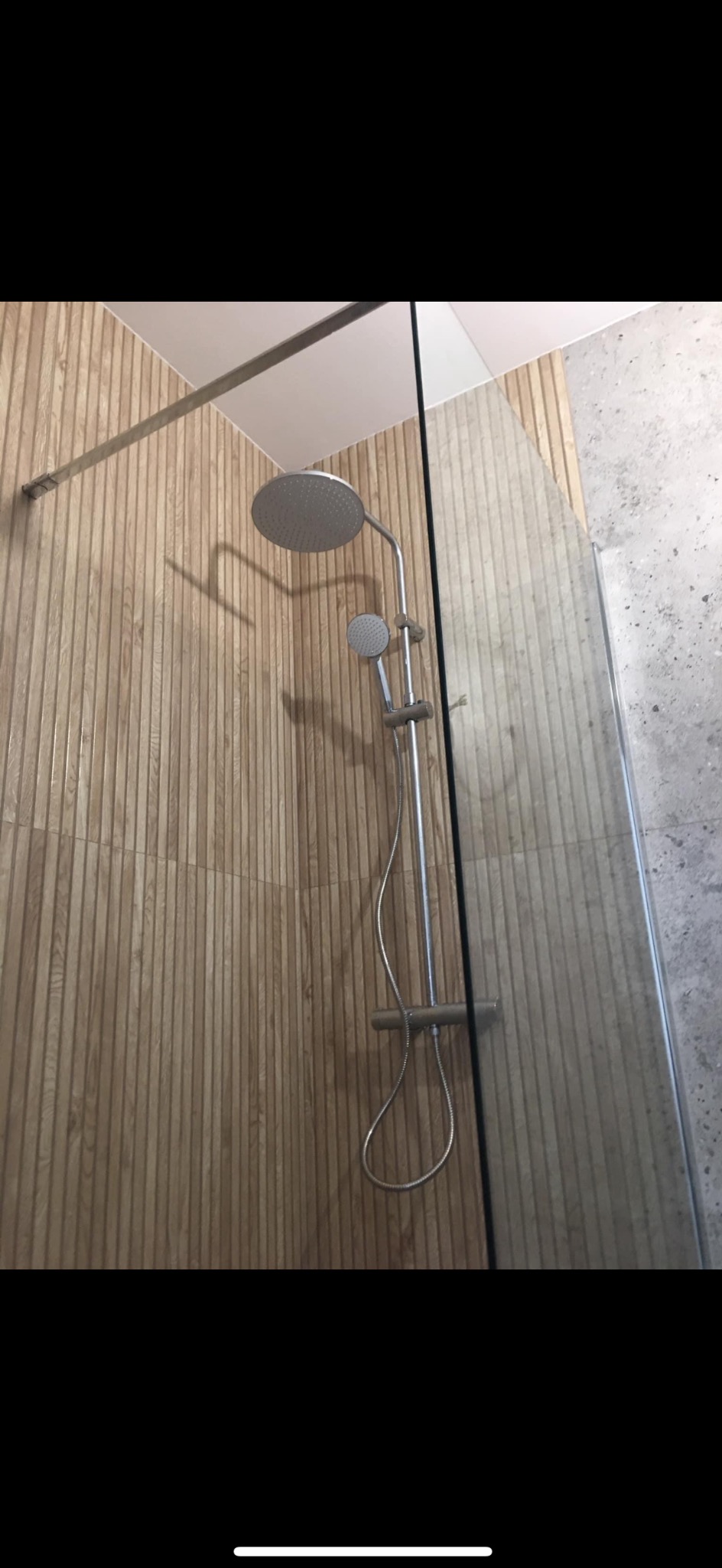 Nowoczesna kabina prysznicowa z deszczownicą i panelem prysznicowym, wykończona płytkami imitującymi drewno na jednej ścianie i szarym kamieniem na drugiej.