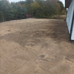 Marcin Czarnecki - Przygotowany teren pod budowę domu jednorodzinnego, widoczne ślady po pracach ziemnych, w tle drzewa i częściowo widoczny czerwony samochód.