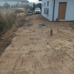 Marcin Czarnecki - Przygotowany teren pod budowę domu jednorodzinnego z widocznymi studzienkami kanalizacyjnymi i częściowo wytyczoną drogą dojazdową. W tle zaparkowany samochód.