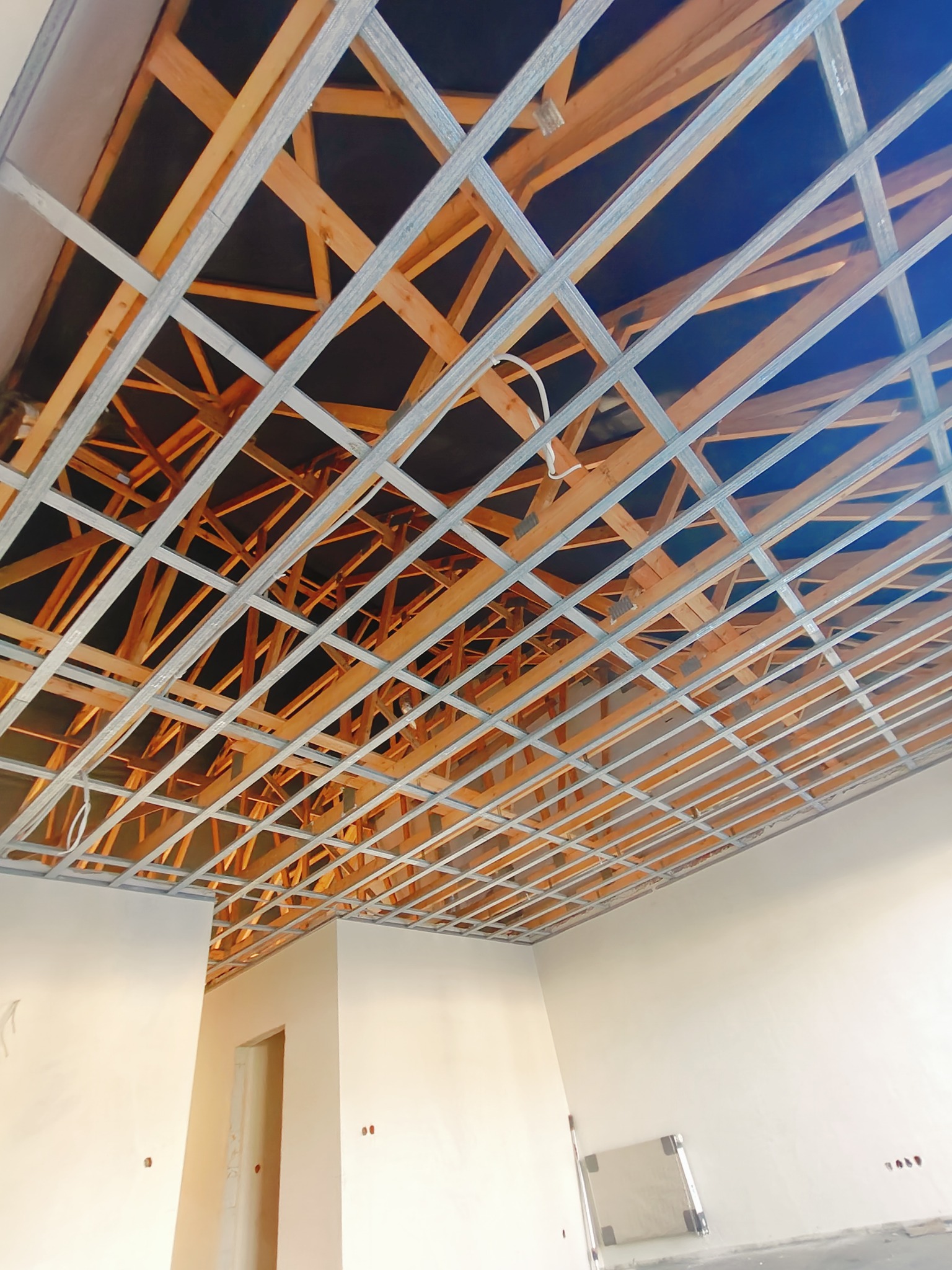 Szkielet sufitu podwieszanego z profili metalowych i drewnianych łat, widok z dołu w surowym wnętrzu.