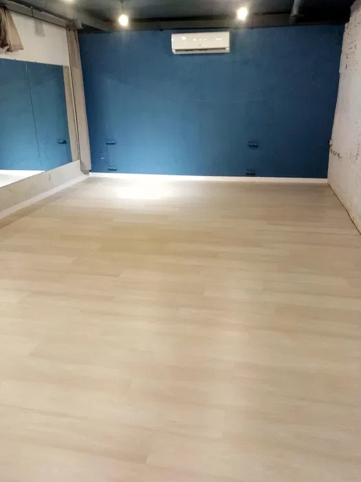 Jasne panele podłogowe w przestronnym pomieszczeniu z niebieską ścianą, widoczne lustro i klimatyzator, surowy, industrialny charakter wnętrza.