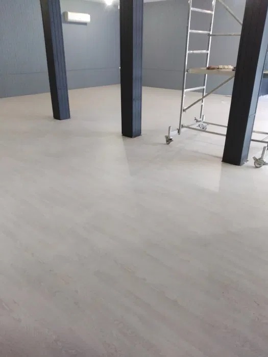 Przygotowane pomieszczenie z jasną, wylaną posadzką, czarnymi filarami i metalowym rusztowaniem, prawdopodobnie przed dalszymi pracami wykończeniowymi.