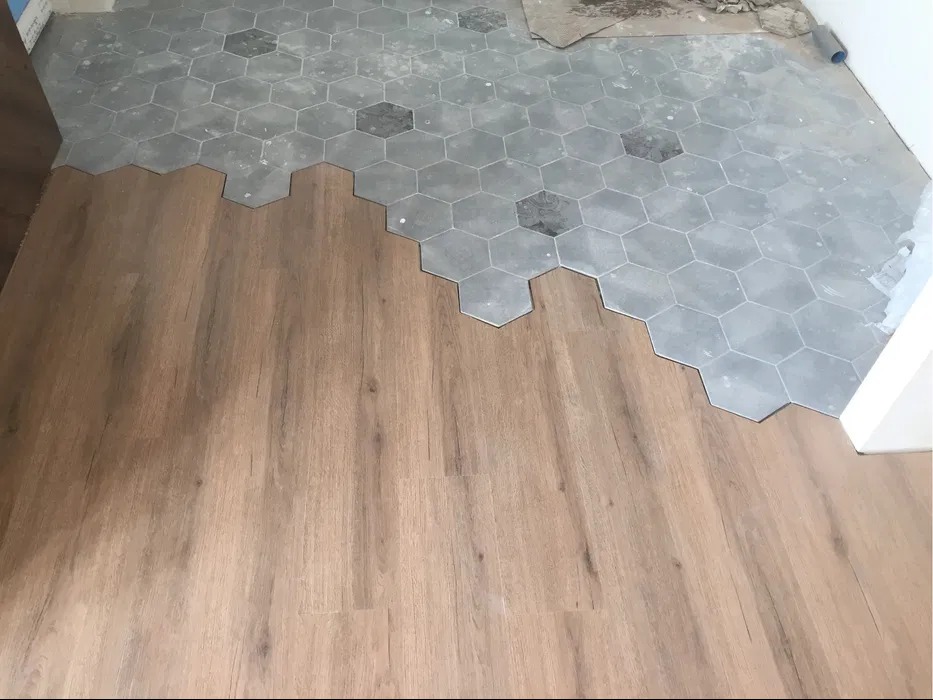 Układanie jasnych paneli podłogowych obok szarych, heksagonalnych płytek podłogowych w trakcie remontu.