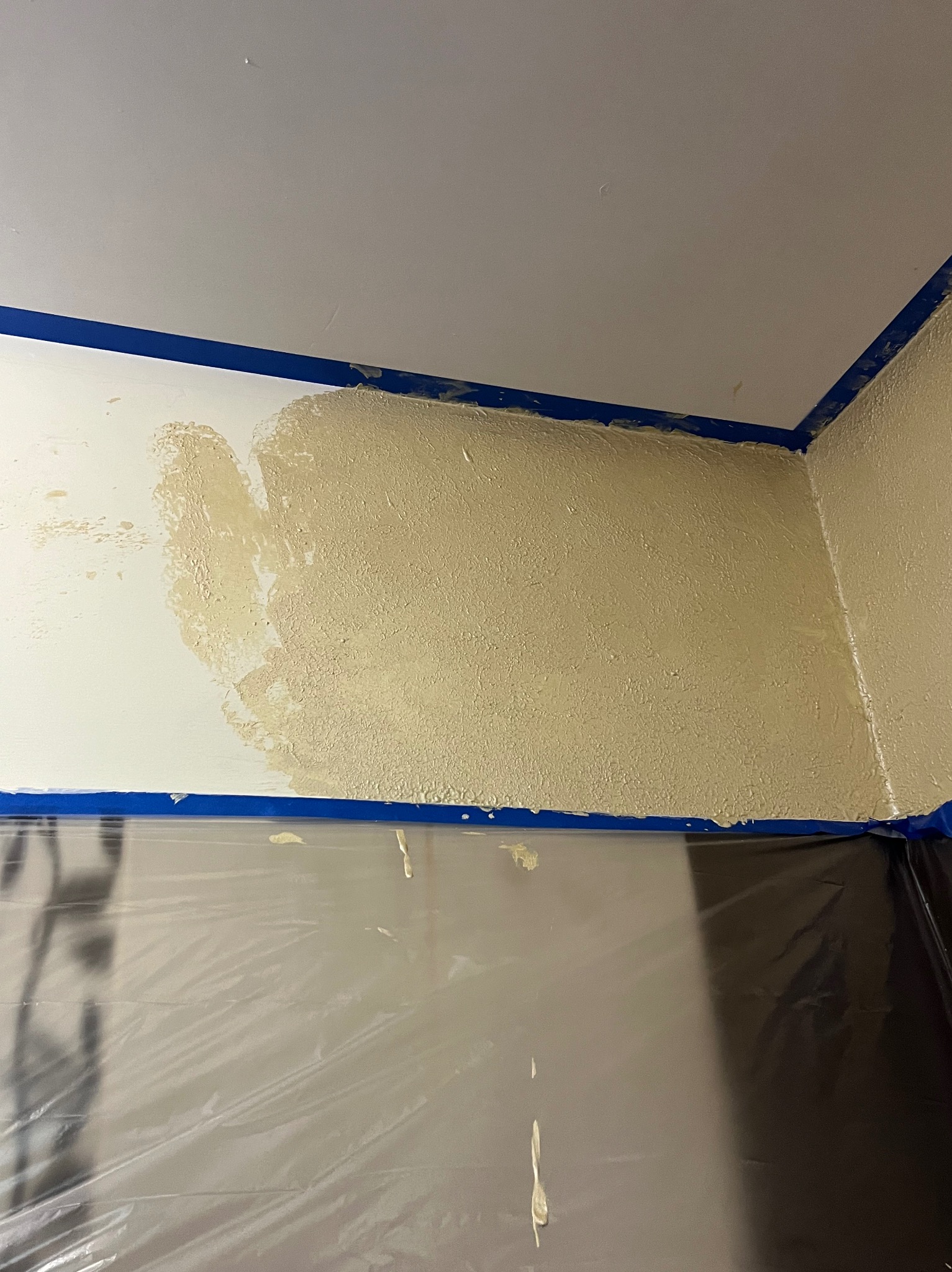 Ściana w trakcie wyrównywania z widocznymi fragmentami nałożonej masy szpachlowej, zabezpieczona folią i taśmą malarską.