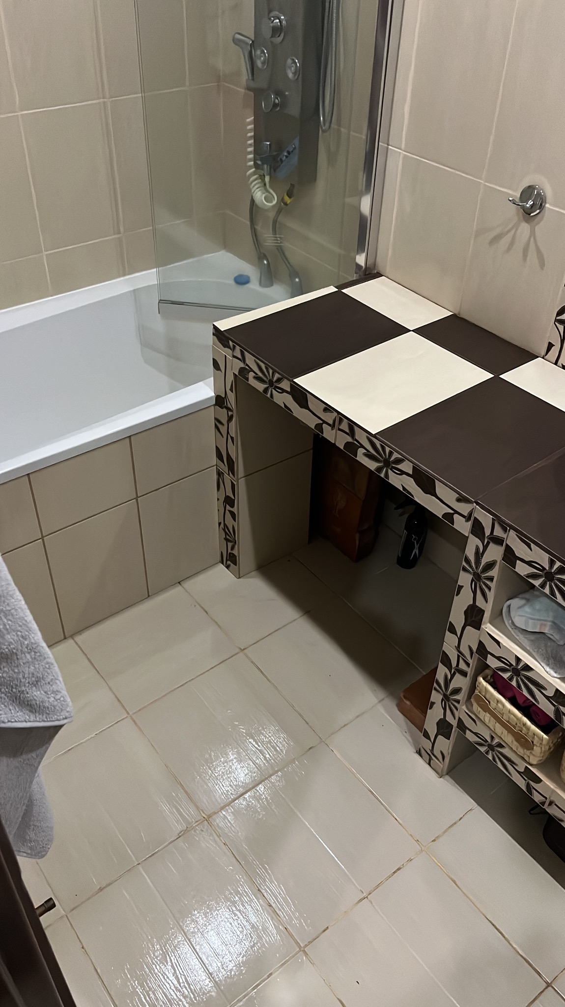 Beżowa łazienka z wanną, kabiną prysznicową i umywalką z blatem w szachownicę, wykończona płytkami w odcieniach beżu.