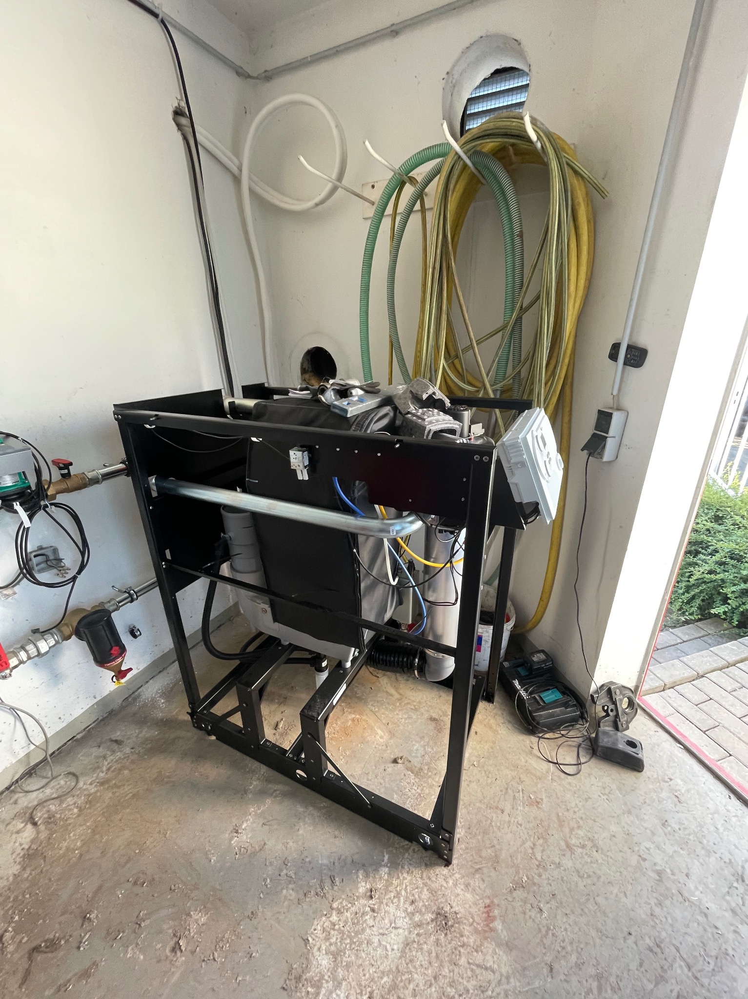 Kompleksowa instalacja uzdatniania wody w metalowej ramie, z widocznymi filtrami, przewodami i osprzętem, zainstalowana w pomieszczeniu technicznym z betonową podłogą i rurami na ścianie.