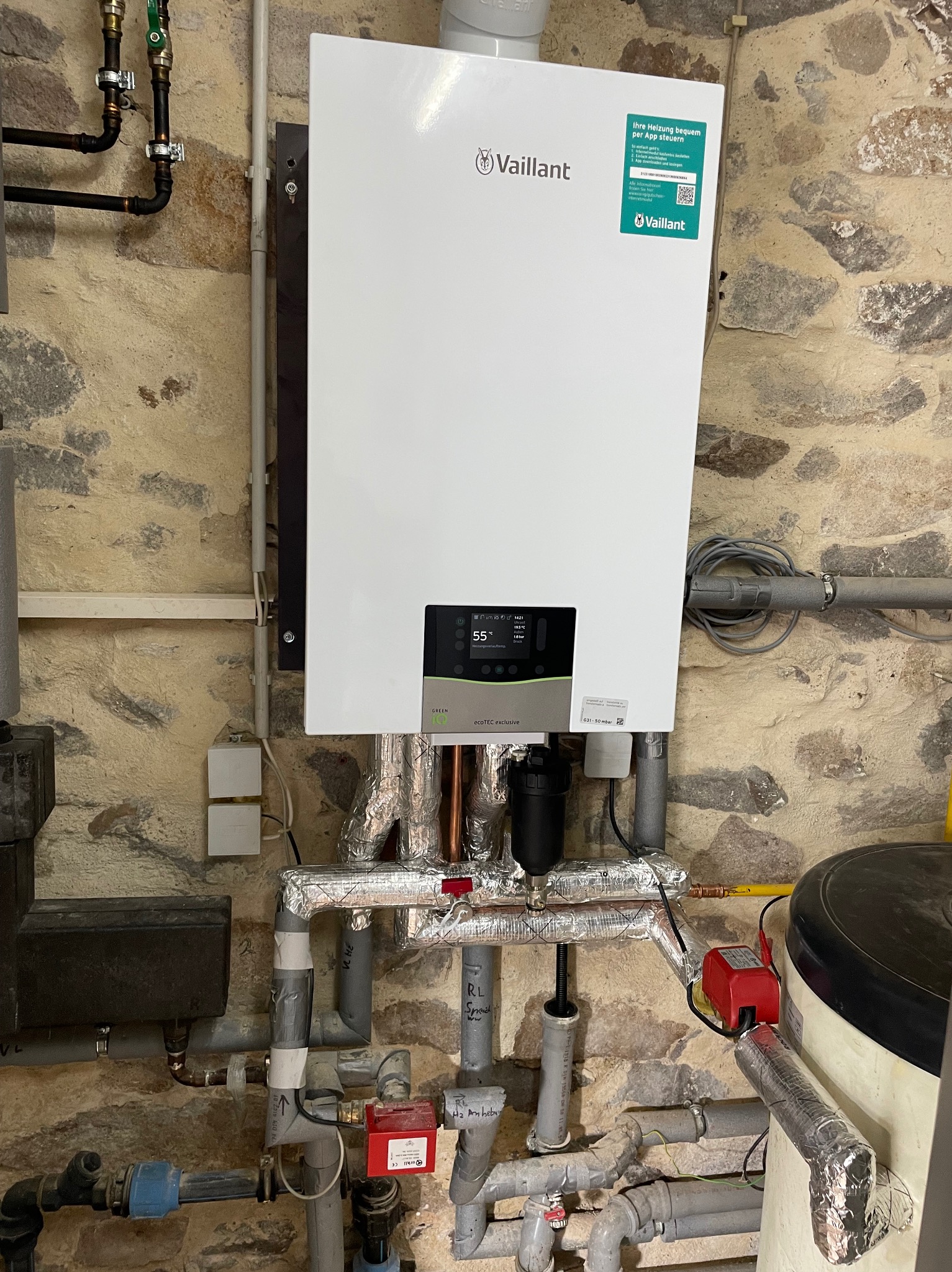 Nowoczesny, biały piec gazowy Vaillant zamontowany na ścianie z kamienia w Książu Wielkopolskim, widoczne rury instalacji grzewczej z izolacją aluminiową.