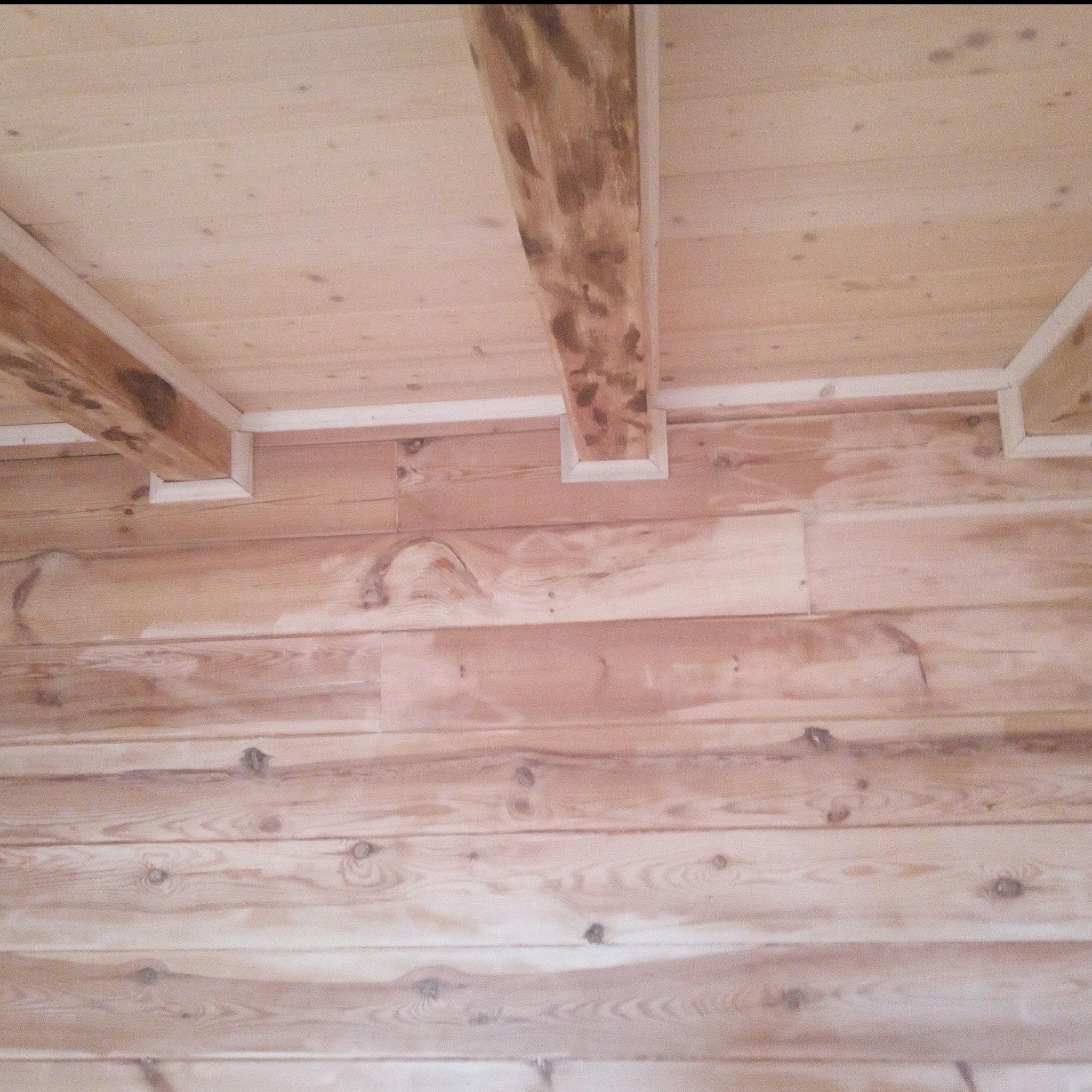 Drewniana boazeria ścienna i sufitowa z widocznymi belkami stropowymi w jasnym odcieniu, wykończona białymi listwami przypodłogowymi.