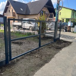 NEX-STAL Łukasz Kurowski - Nowoczesna, ciemnoszara brama panelowa z widocznym znakiem ostrzegawczym 'GAZ' i narzędziami do montażu, na tle domu z beżową elewacją i białym dostawczym samochodem.