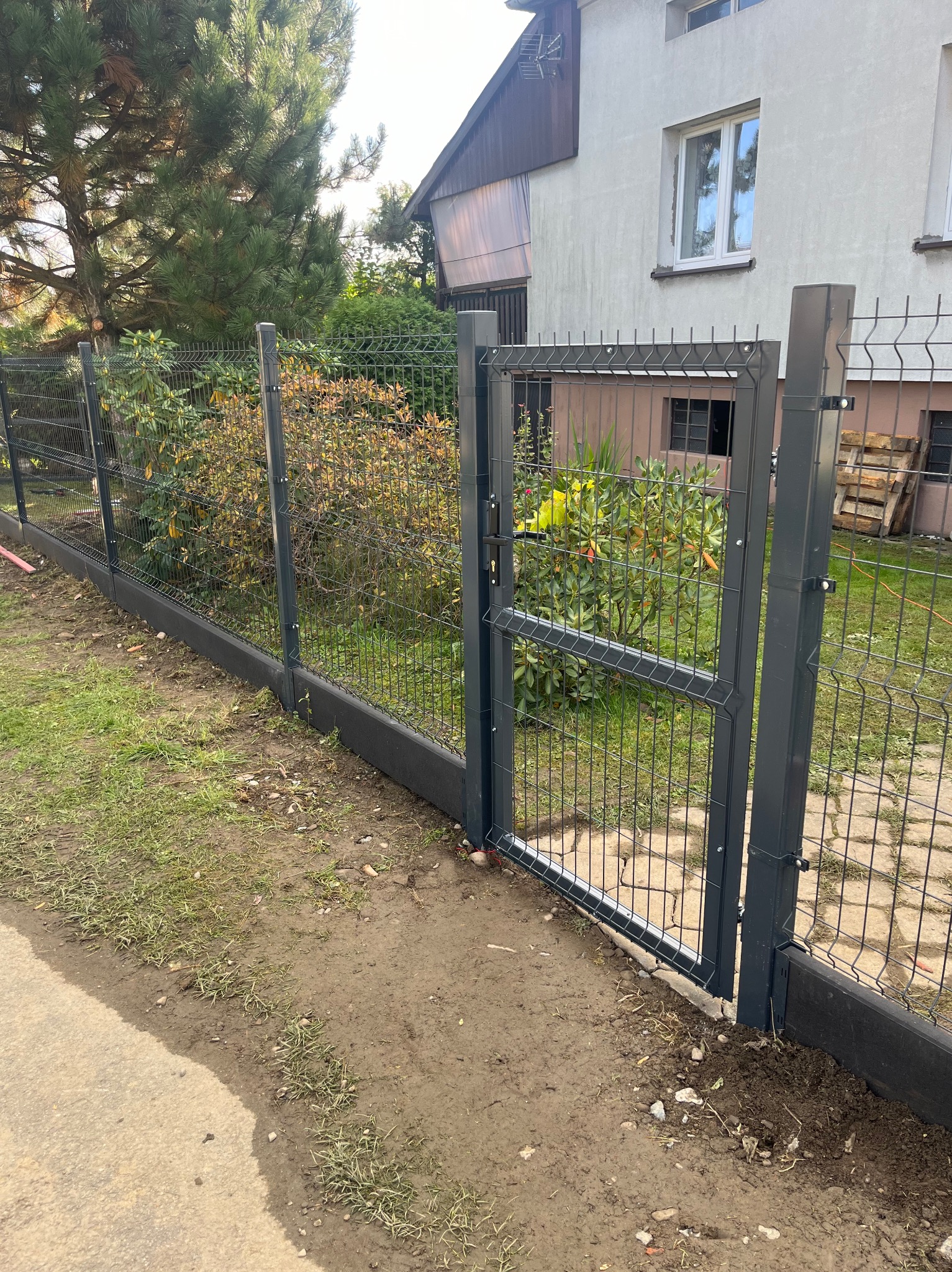 Panelowe ogrodzenie z furtką na posesji w Pietrzykowicach, z widocznymi elementami montażowymi i betonową podmurówką.