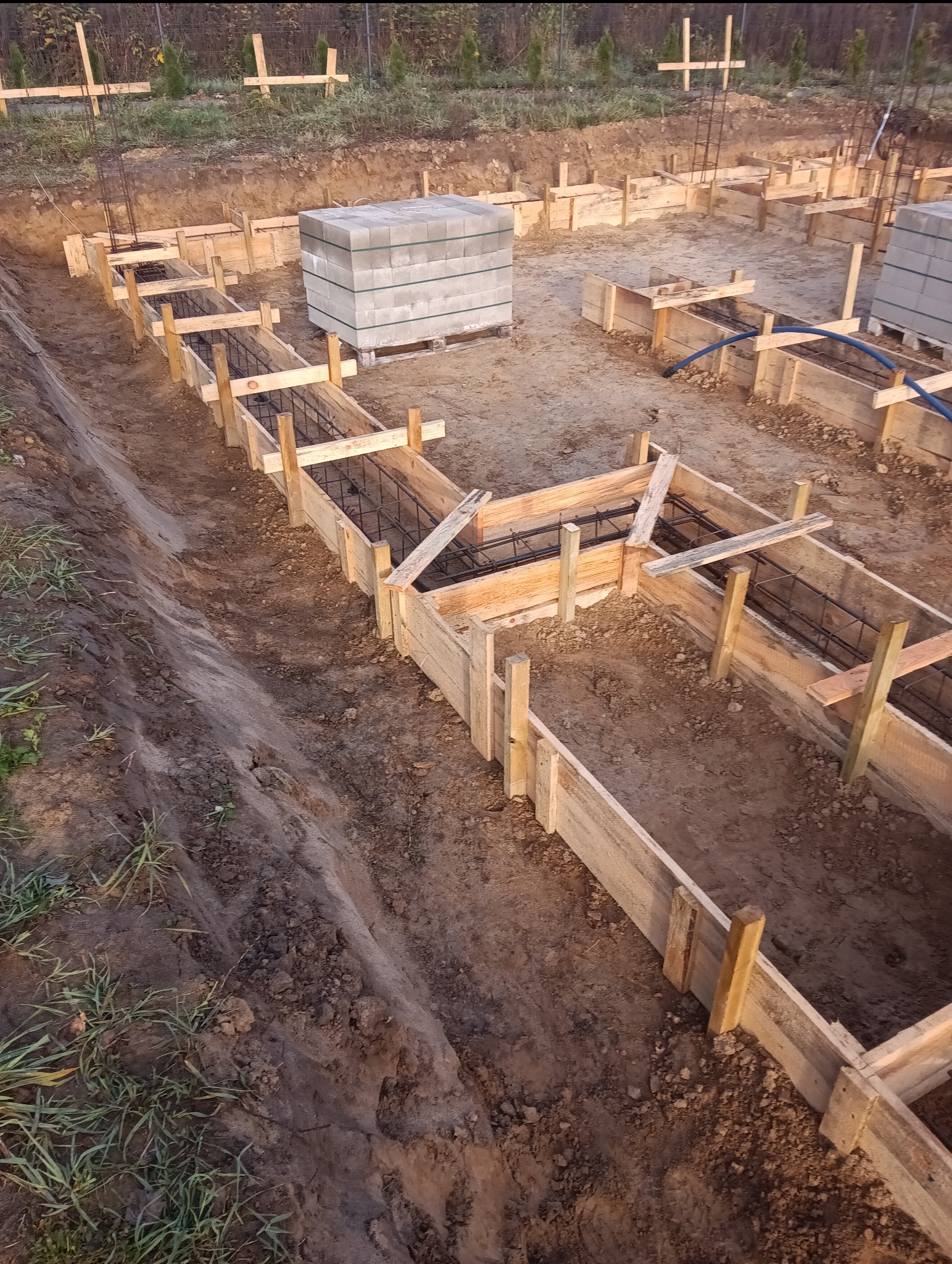 Przygotowanie szalunków zbrojeniowych pod fundament domu jednorodzinnego, widoczne zbrojenie oraz paleta z bloczkami betonowymi.