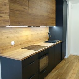 MB - meble - Nowoczesna kuchnia: czarne szafki z drewnianym blatem i górnymi szafkami z forniru. Złota bateria, płyta indukcyjna i oświetlenie LED pod szafkami.