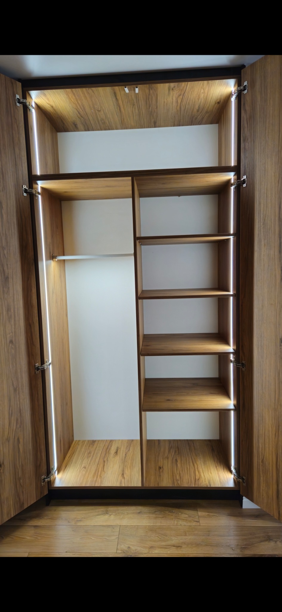 Otwarta szafa wnękowa z oświetleniem LED, drewnopodobne wykończenie, półki i drążek na ubrania. Widok z przodu, wnętrze szafy.