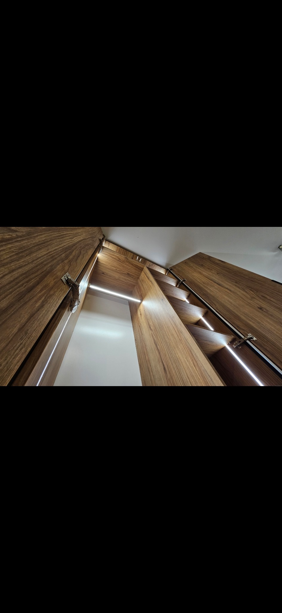 Wnętrze szafy z drewnianymi półkami i oświetleniem LED, widok z dołu, ukazujący precyzję wykonania i nowoczesny design.