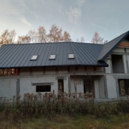 Piotr Malejka - Surowy budynek w trakcie budowy z nowym, grafitowym dachem z blachy trapezowej i trzema oknami dachowymi, widok z zewnątrz na tle drzew.