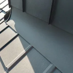 Szczegółowe ujęcie połączenia obróbki blacharskiej z panelami dachowymi w kolorze grafitowym, widoczne cieniowanie i faktura materiałów.