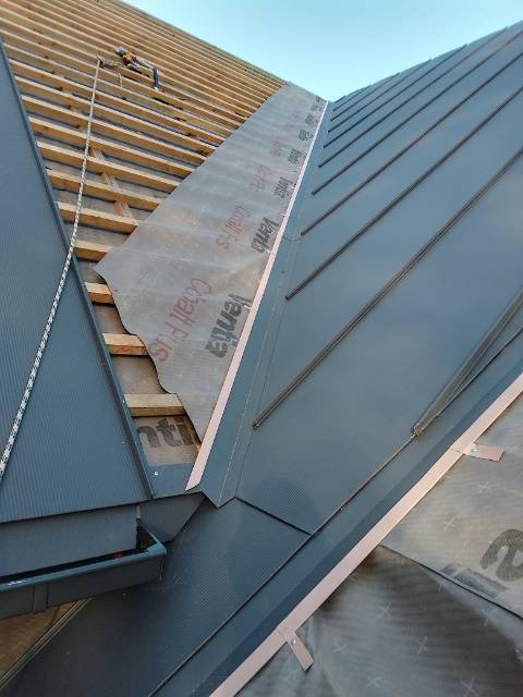 Montaż blachy na rąbek stojący na dachu, widoczna membrana dachowa Venti, drewniana konstrukcja więźby dachowej oraz narzędzia dekarskie na dachu.