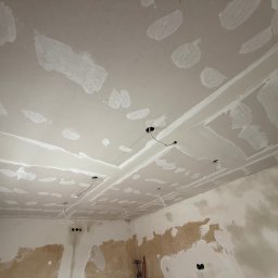 Dawid Kliczkowski - Sufit z płyt gipsowo-kartonowych w trakcie szpachlowania, widoczne otwory na oświetlenie i fragmenty ścian z pozostałościami starej farby.