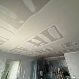 Dawid Kliczkowski - Sufit po szpachlowaniu z widocznymi łatami i zabezpieczonymi folią ścianami, przygotowany do dalszych prac wykończeniowych.