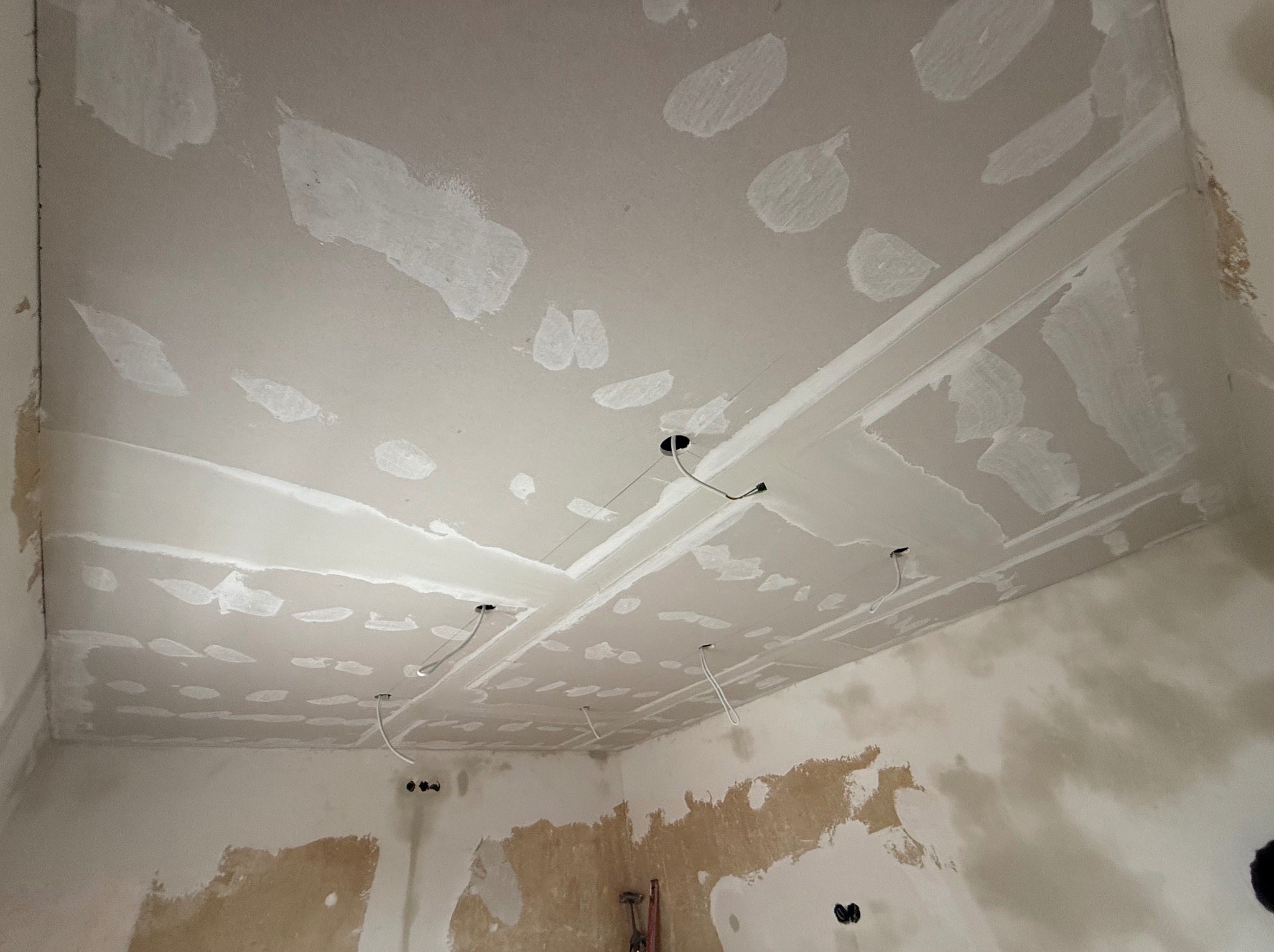 Sufit z płyt gipsowo-kartonowych w trakcie szpachlowania, widoczne otwory na oświetlenie i fragmenty ścian z pozostałościami starej farby.