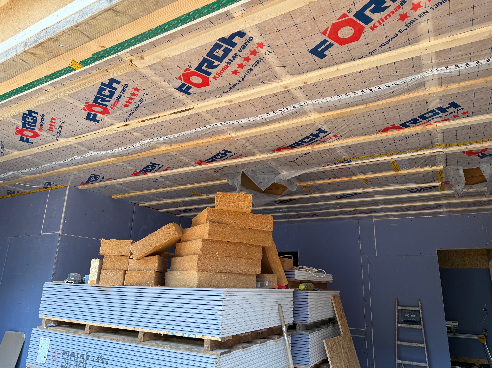 Wnętrze w trakcie prac wykończeniowych: ułożone płyty karton-gips, izolacja stropu z folią paroizolacyjną FORCH, wełna mineralna, drabina. Widok z dołu.