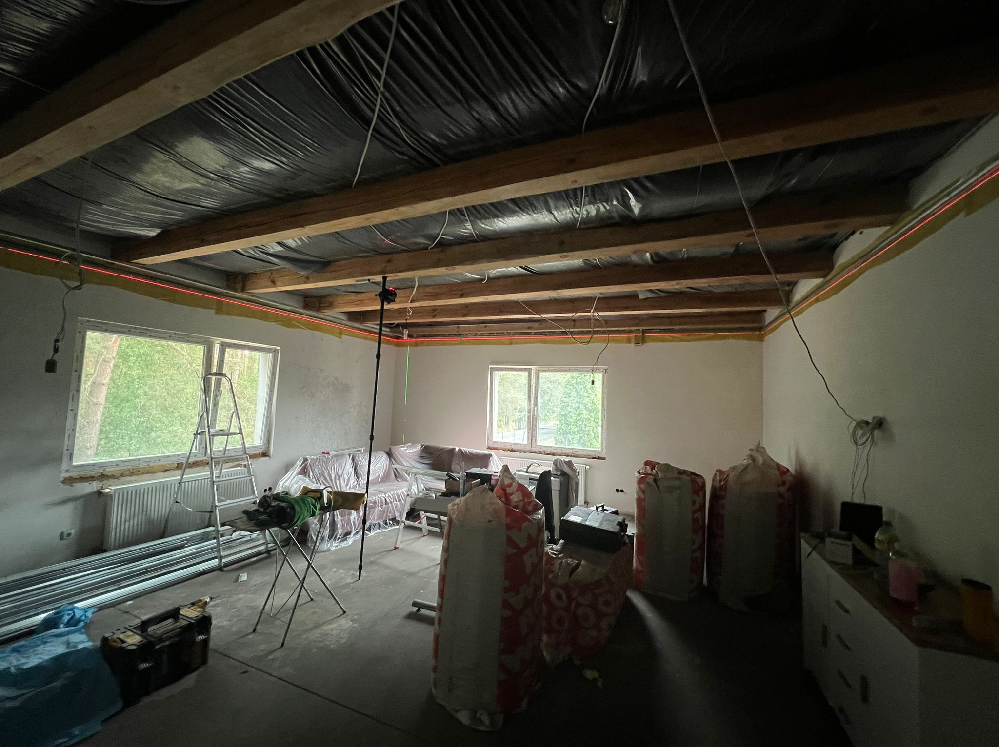 Montaż sufitu podwieszanego w Stargardzie. Widoczne profile, folia i laser krzyżowy wyznaczający poziom. Prace w toku, pomieszczenie częściowo zabezpieczone folią.