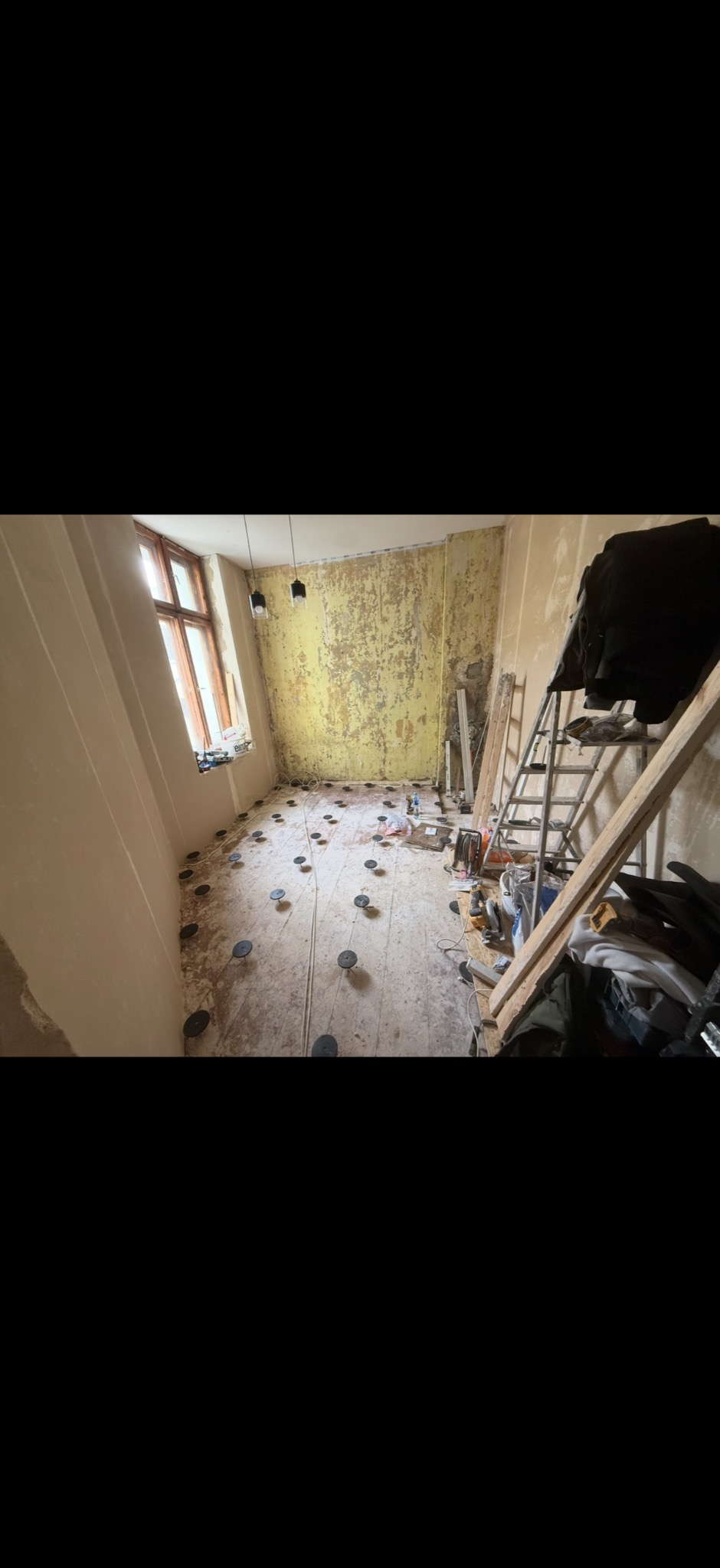 Pokój w trakcie remontu: przygotowanie podłoża pod panele z widocznymi wspornikami, ściany częściowo otynkowane, drabina i narzędzia w tle.