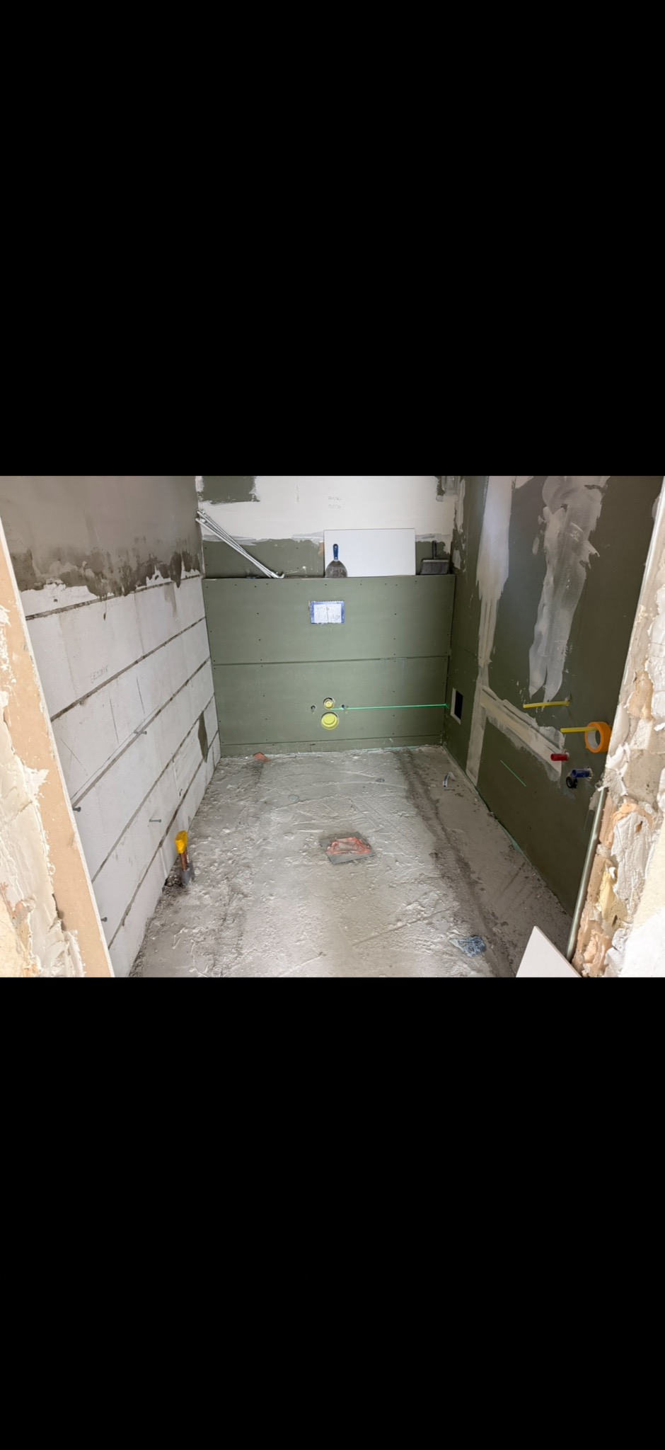 Łazienka w trakcie remontu: ściany z płyt karton-gips, widoczne instalacje, podłoga przygotowana pod wylewkę. Laserowy niwelator wyznacza poziom.