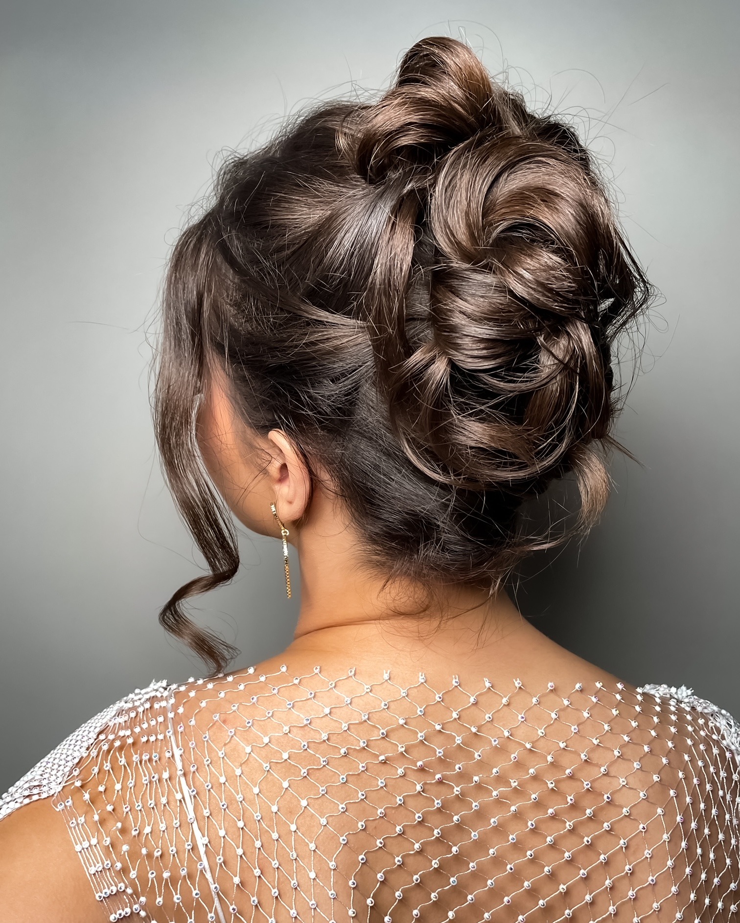Elegancka fryzura upięta z brązowych włosów, widok z tyłu, z delikatnym upięciem i pojedynczym, zwisającym kolczykiem