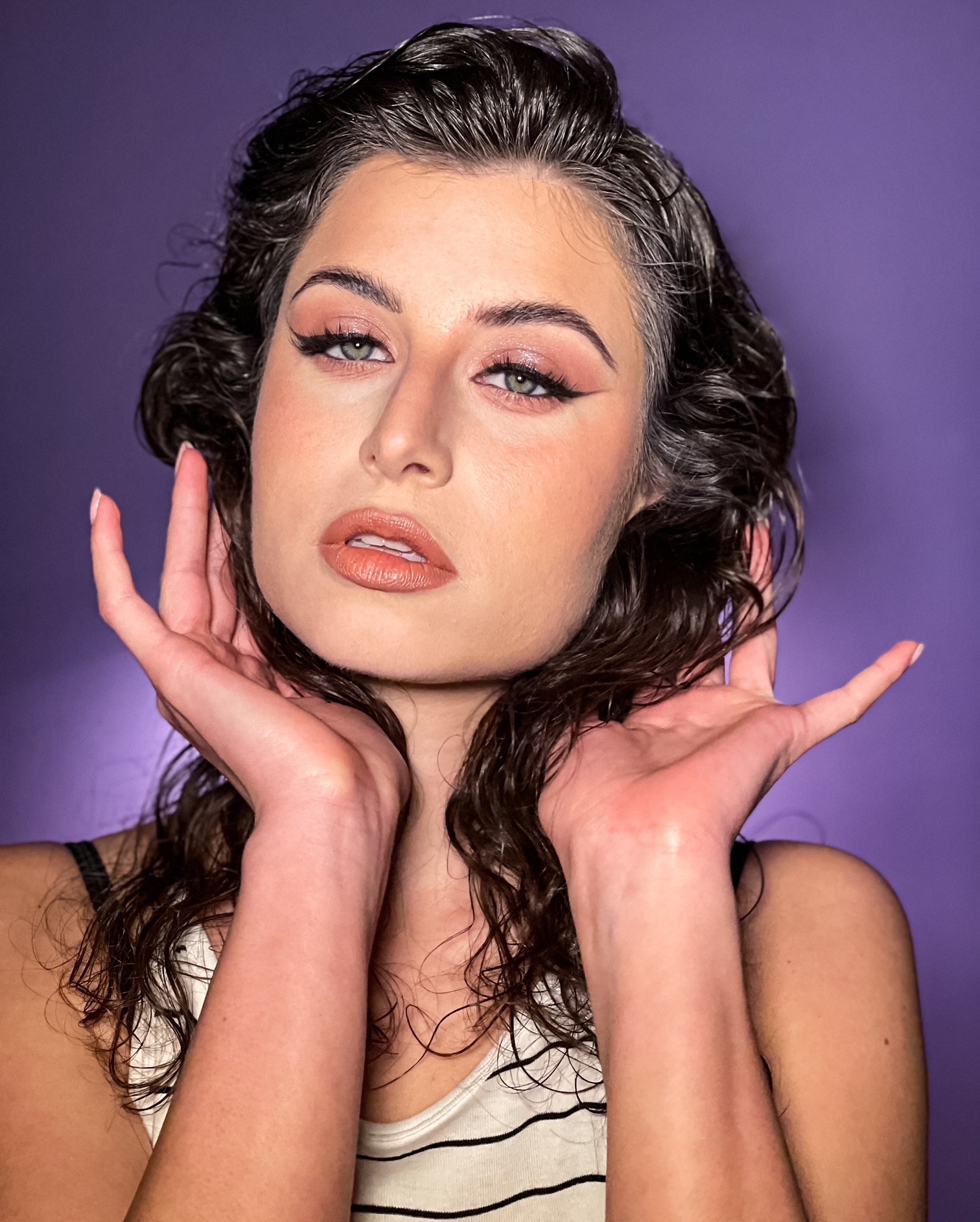 Portret kobiety ze świeżym, profesjonalnym makijażem w stylu glamour, wykonanym w Szczecinie, z uwydatnionymi oczami i błyszczącymi ustami na fioletowym tle. Włosy po stylizacji, delikatnie...