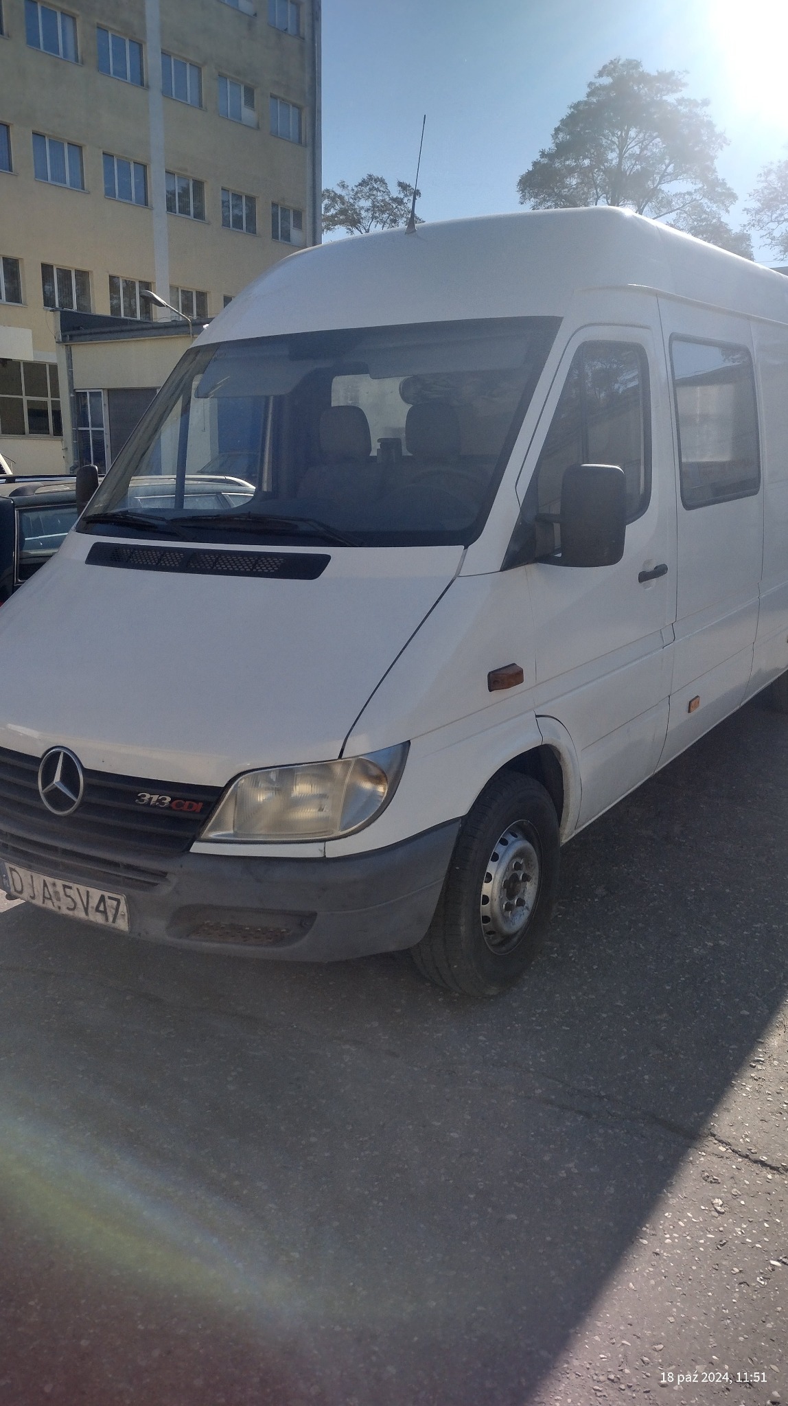 Biały bus Mercedes-Benz Sprinter 313 CDI zaparkowany na zewnątrz budynku, widoczny z przodu pod lekkim kątem.