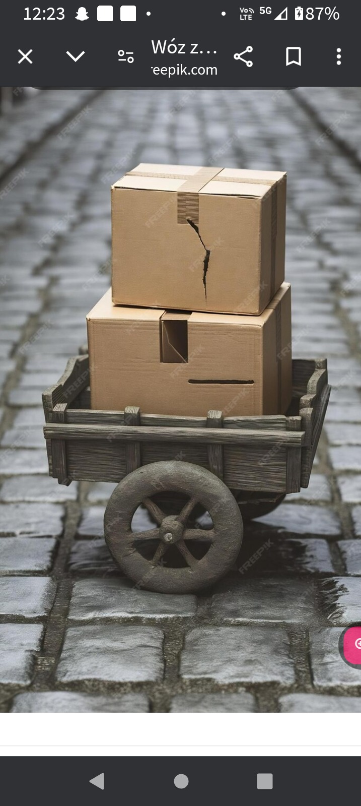 Dwa kartonowe pudła na drewnianym wózku z jednym kołem, stojącym na brukowanej ulicy; górne pudełko ma pęknięcie na boku.