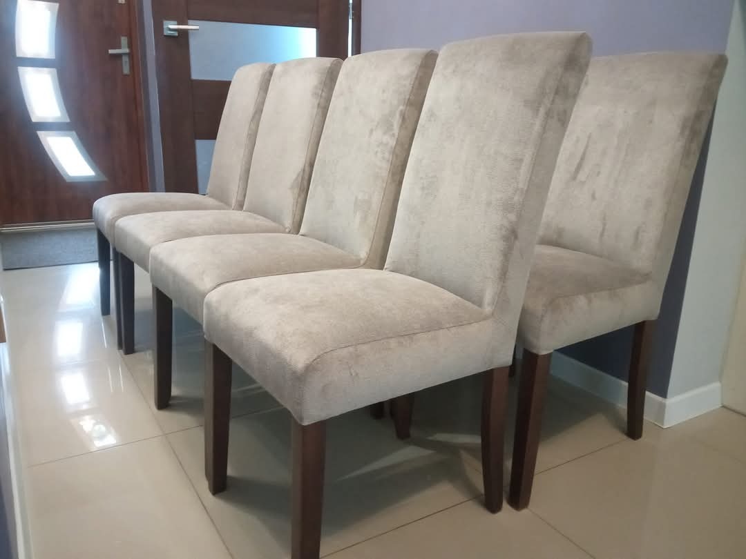 Rząd pięciu krzeseł z beżową tapicerką i ciemnymi nogami, ustawionych na błyszczącej podłodze. W tle widoczne drzwi z nowoczesnym wzorem.