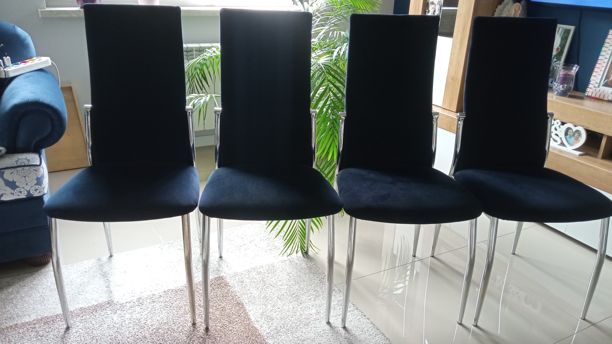 Cztery krzesła po renowacji tapicerskiej w Wilczkowicach Górnych. Ciemny, welurowy materiał obiciowy i chromowane nogi. Widoczny fragment wnętrza.