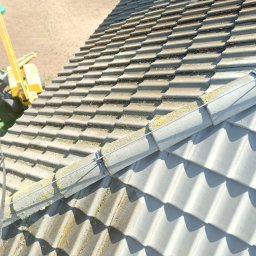 Czysta Strefa Mateusz Wójcik - Częściowy widok na dachówkę z mchem i zabrudzeniami, z żółtym podnośnikiem w tle. Fragment dachu po czyszczeniu, ukazujący różnicę w kolorze.