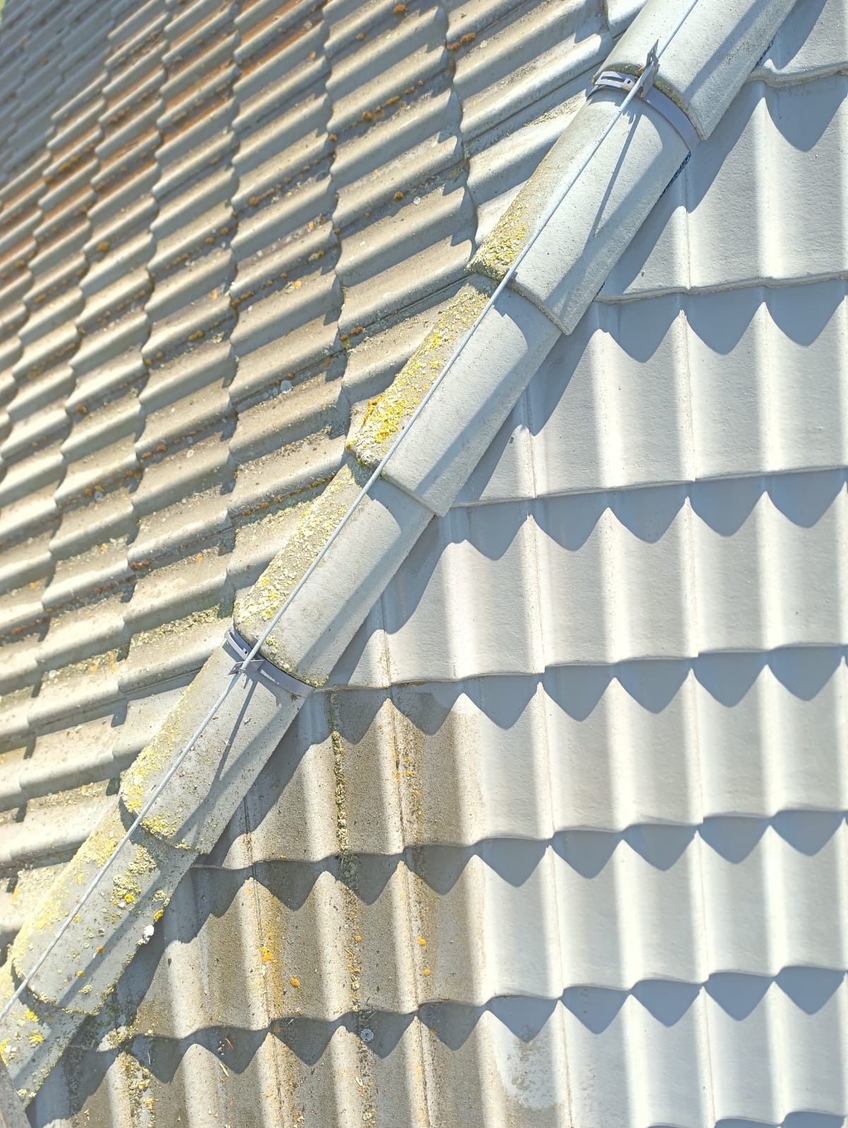 Fragment dachu z dachówką, widoczny podział na czystą i zabrudzoną część, ukazujący efekt mycia. Zarys dachu z wyraźnym cieniem.