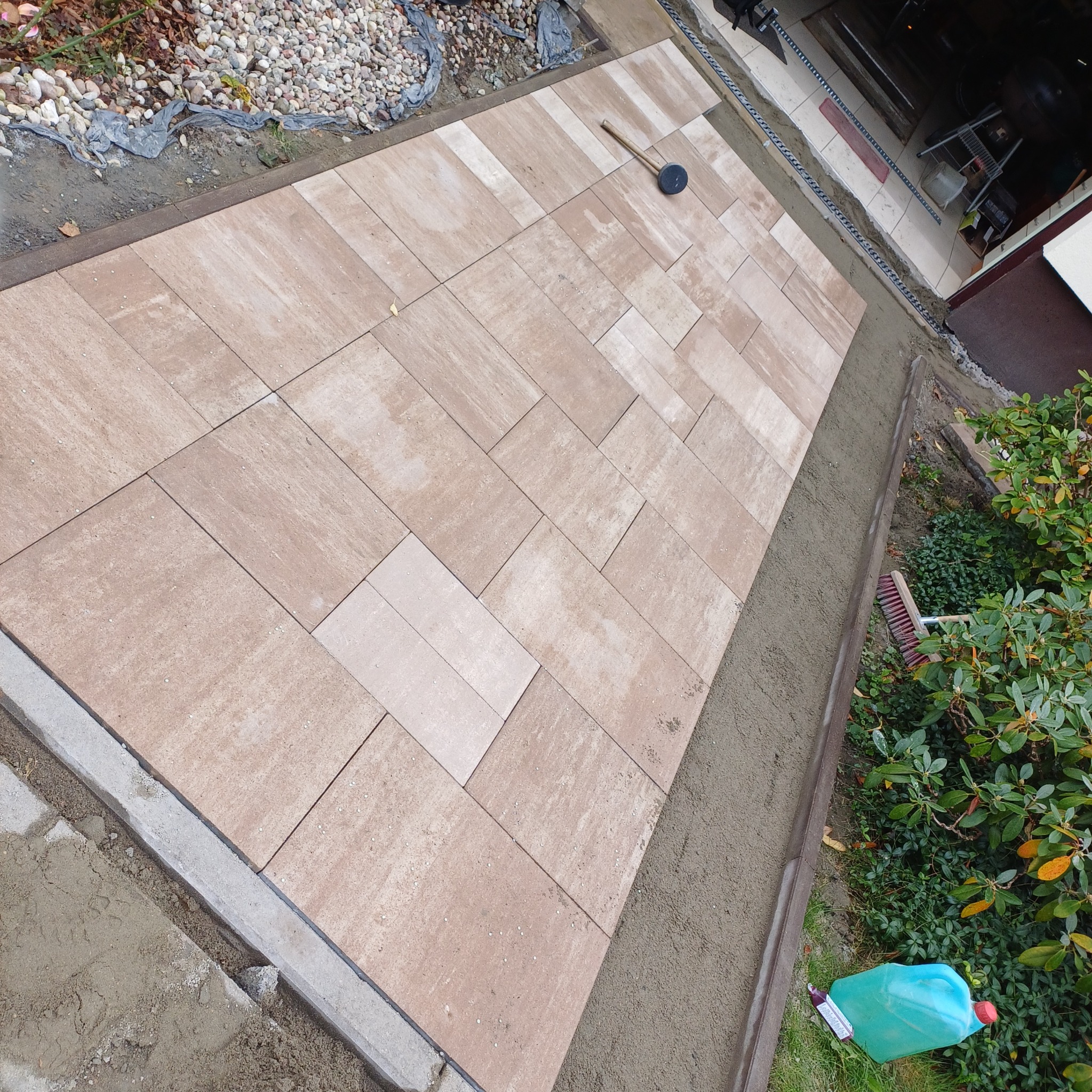 Ułożona beżowa kostka brukowa na posesji, widoczny gumowy młotek, obrzeża oraz piasek do fugowania.
