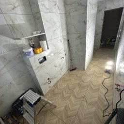 Bruinvest Tomasz Brucki - Ułożone wielkoformatowe płytki ścienne imitujące marmur oraz podłogowe w jodełkę w łazience, z widoczną wnęką i narzędziami budowlanymi.