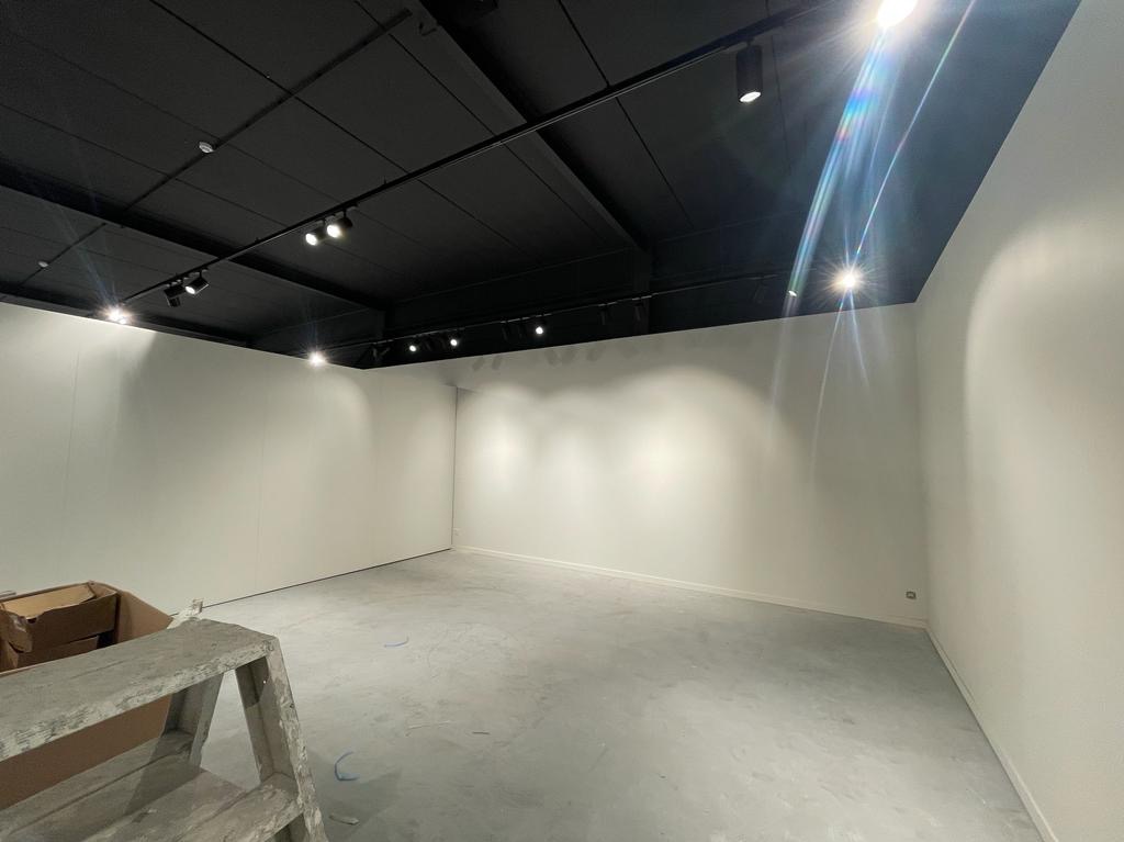 Wnętrze lokalu po remoncie z zamontowanym oświetleniem punktowym na czarnym suficie, widoczne białe ściany i szara podłoga, kartony oraz drabina malarska w rogu.