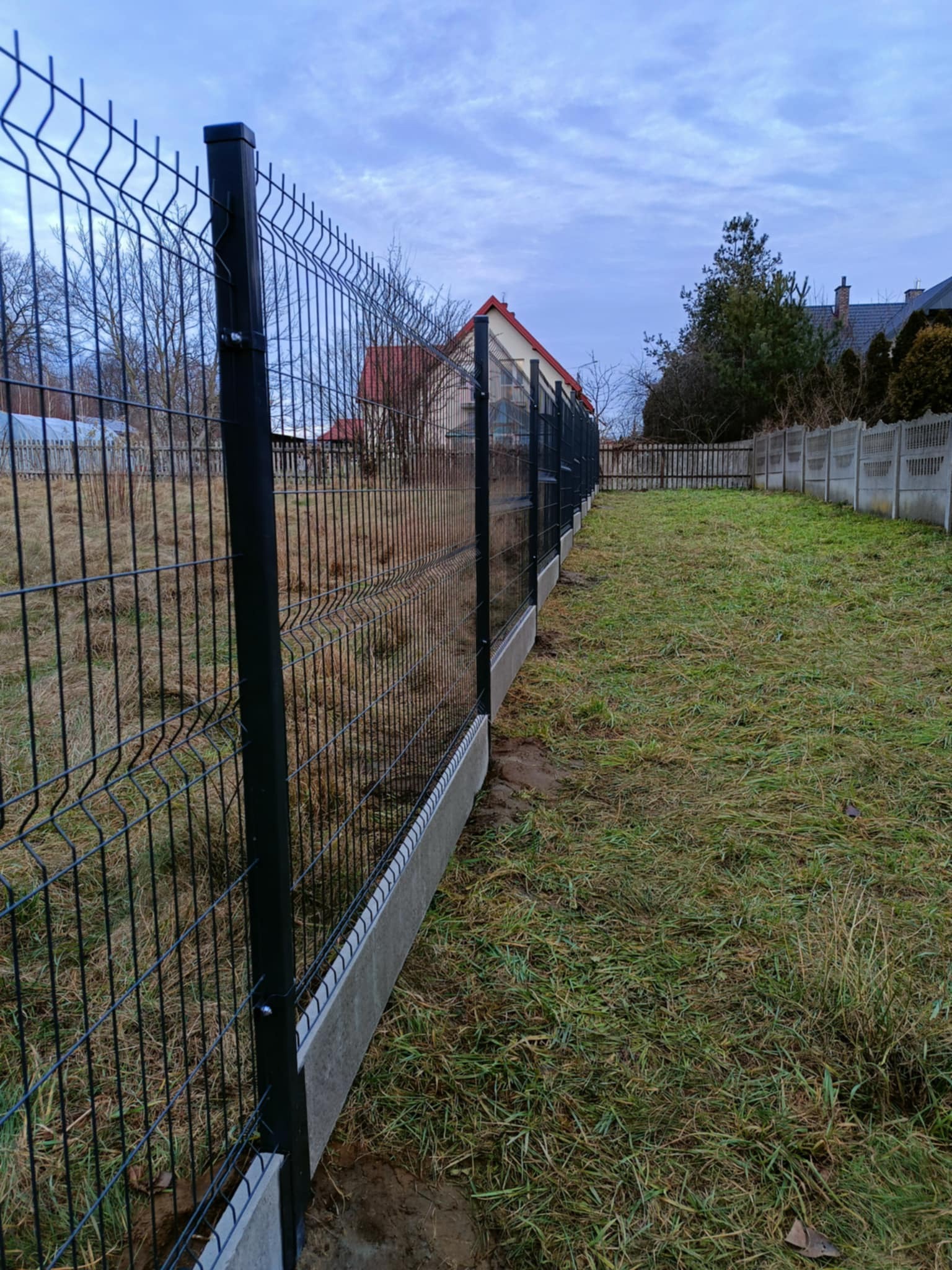 Nowoczesne ogrodzenie panelowe z podmurówką betonową, widok z perspektywy trawnika w pochmurny dzień.